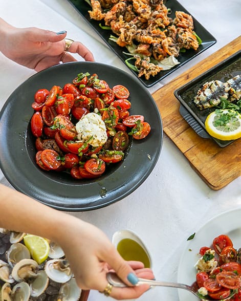 Hands serving a cherry tomato salad with white cheese on a black plate