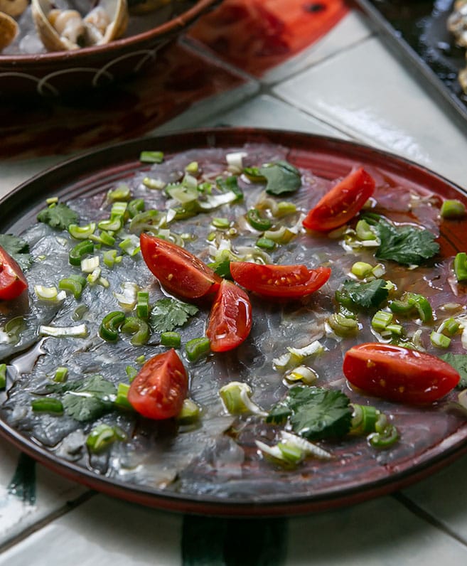 Thin slices of raw fish with cherry tomatoes on a red plate