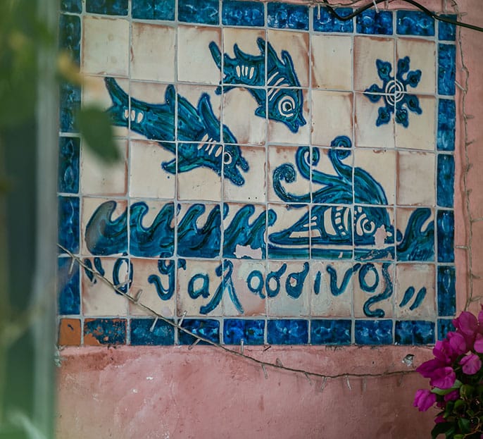The blue-and-white fish tile mural with the name Ο Θαλασσινός on the pink outside wall of the taverna