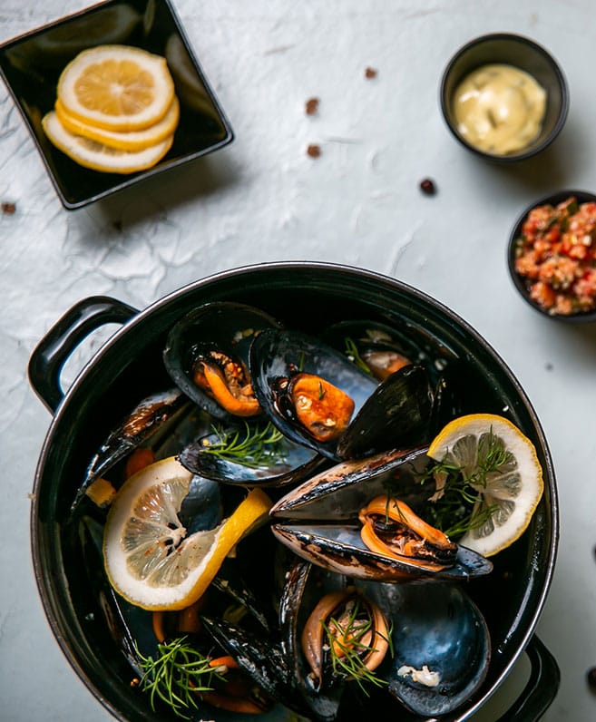 Steamed mussels in a black pot with a wedge of lemon