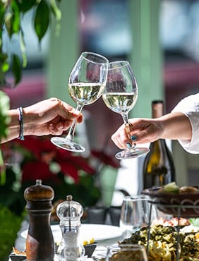 Two glasses of white wine clinking in a toast, red flowers behind